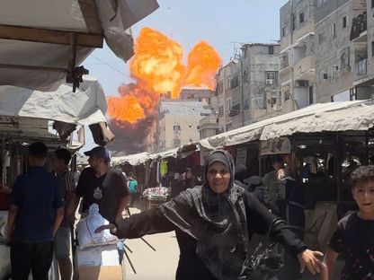 فلسطينيون يحاولون الحصول على بعض المواد الغذائية بينما تبدو النيران مشتعلة جراء غارة إسرائيلية على منزل في مدينة غزة بشمال القطاع. 1 يونيو 2025 - REUTERS