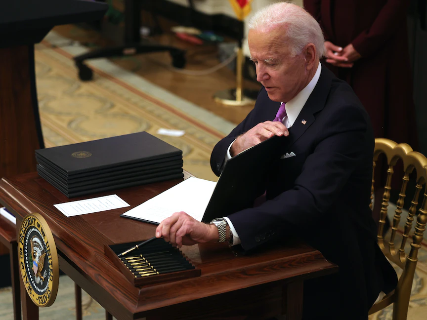 الرئيس الأميركي جو بايدن يتناول قلماً للتوقيع على أمر تنفيذي، 21 يناير 2021 - AFP