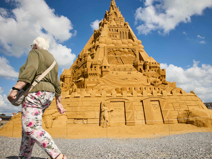 امرأة تمشي أمام أطول قصر رملي في العالم في بلوخوس بالدنمارك - 7 يوليو 2021 - AFP