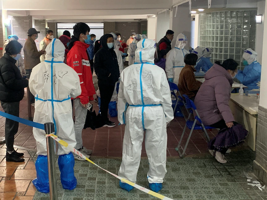 عاملون طبيون يرتدون بدلات واقية يقفون بجانب السكان الذين ينتظرون الفحص بعد تفشي مرض فيروس كورونا (COVID-19) في شنغهاي، الصين - 20 مارس 2022 - REUTERS