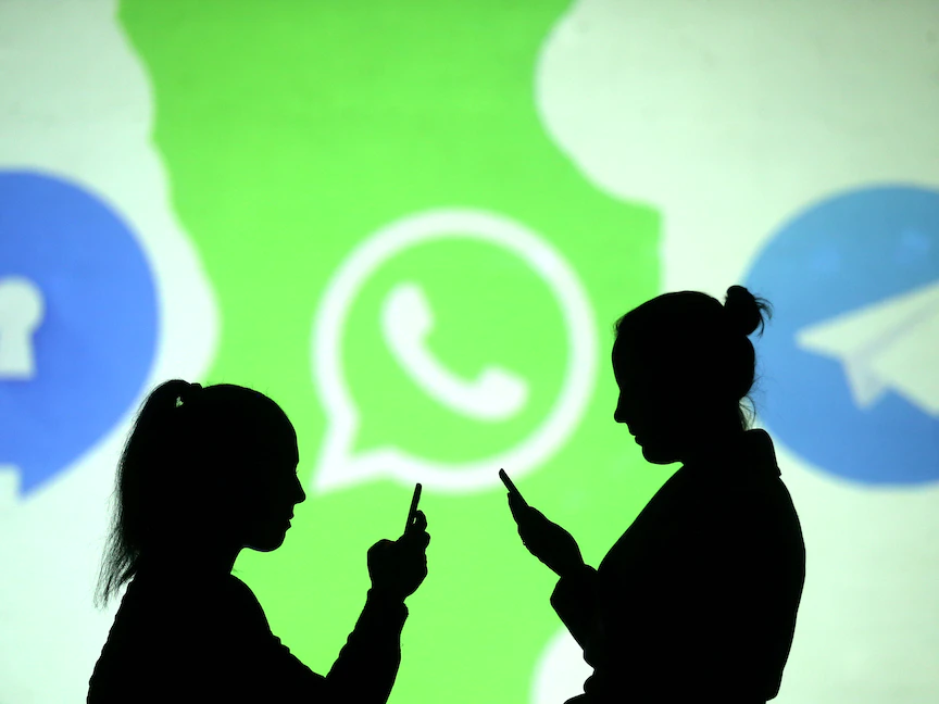 سيدتان تمسكان هاتفيهما أمام شعارات تطبيقات التراسل الفوري سيغنال وواتساب وتليغرام - REUTERS