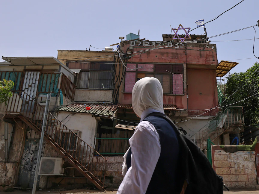 فتاة فلسطينية تنظر إلى منزل رفع فوقه علم إسرائيلي في حي الشيخ جراح بالقدس المحتلة 5 مايو 2021 - AFP