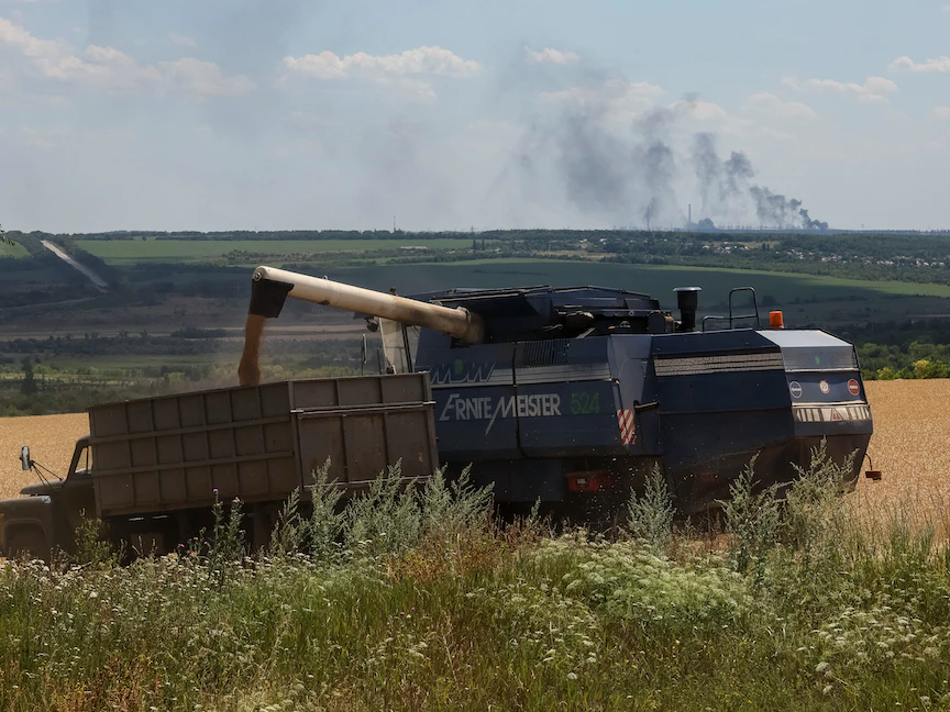 مزارعون يحصدون القمح في الوقت الذي تحترق فيه محطة فولهيرسك لتوليد الطاقة الحرارية بمنطقة دونباس بأوكرانيا - 18 يوليو 2022 - REUTERS