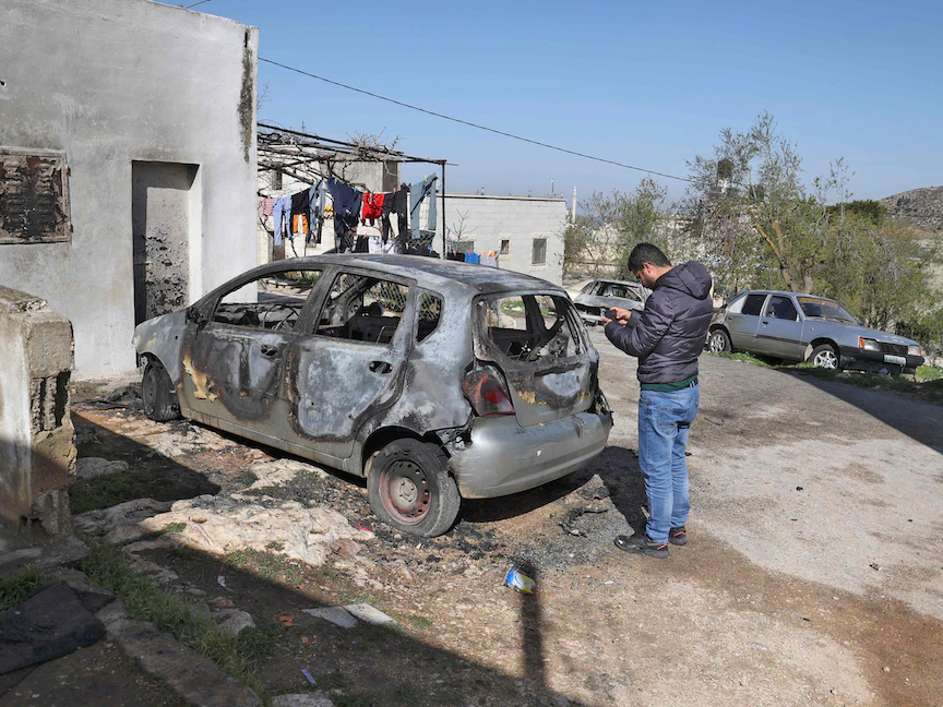 فلسطيني يفحص ما تبقى من سيارته التي أحرقها مستوطنون يهود أمام منزله في قرية جالود جنوب نابلس بالضفة الغربية- 28 مارس 2022 - AFP