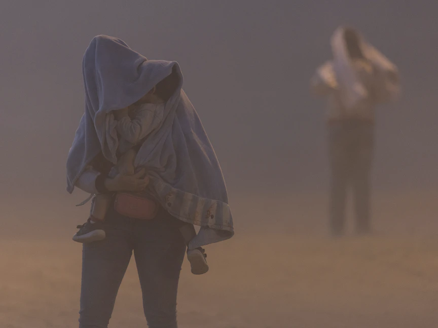 أم مهاجرة مع طفلها تسير خلال عاصفة رملية بين الحدود الأميركية والمكسيكية، 10 مايو 2023 - Getty Images via AFP