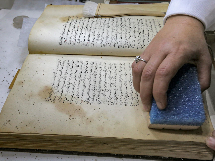أخصائية ترميم تستخدم إسفنجة على مخطوطة باللغة الفارسية في معمل بيت المخطوطات العراقي - بغداد - 6 ديسمبر 2022 - AFP