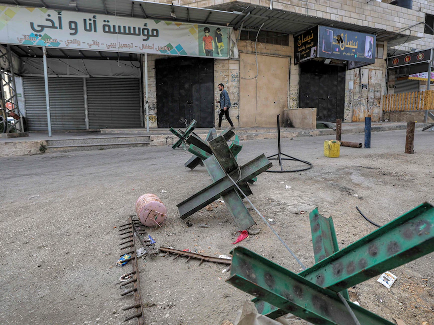 رجل يسير أمام محلات مغلقة وحواجز في طريق بمخيم جنين خلال إضراب احتجاجاً على مقتل 6 فلسطينيين خلال اقتحام المخيم، الضفة الغربية المحتلة. 8 مارس 2023 - AFP