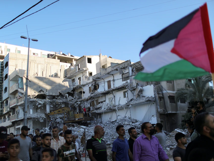 فلسطينيون يسيرون أمام مبنى دمرته الغارات الجوية الإسرائيلية أثناء مشاركتهم في احتجاج على مسيرة رفع الأعلام في البلدة القديمة بالقدس الشرقية، شمالي قطاع غزة، 15 يونيو 2021 - REUTERS