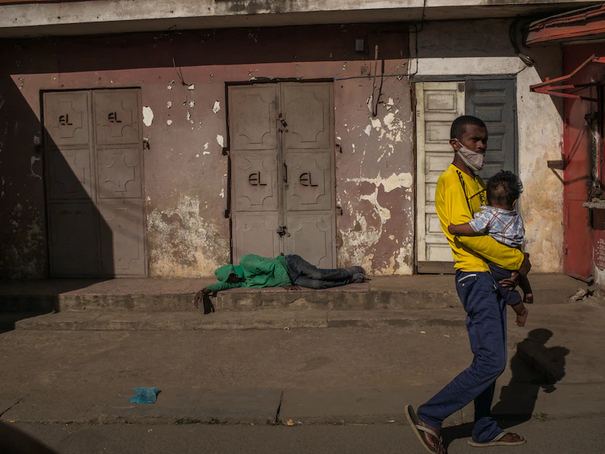 رجل يحمل طفلاً في شارع مهجور ومغلق في عاصمة مدغشقر أنتاناناريفو - 24 أبريل 2021 - AFP