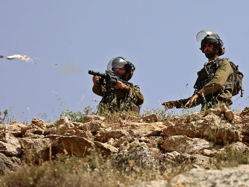 عنصران من القوات الإسرائيلية يوجهان سلاحيهما نحو متظاهرين فلسطينيين في بيت دجن شرق نابلس بالضفة الغربية المحتلة- 29 أبريل 2022 - AFP