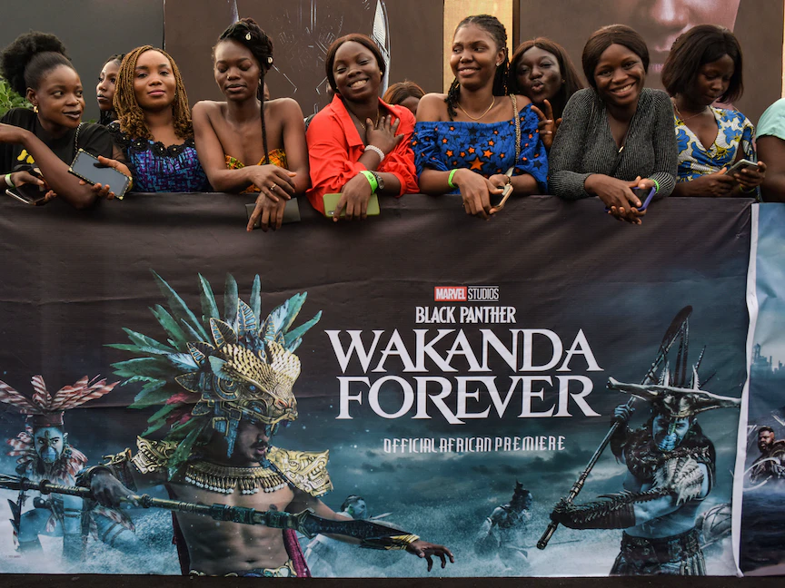 مشاهدون يتكئون على إعلان فيلم "Black Panther: Wakanda Forever" في انتظار دخول صالة العرض الأول للفيلم في لاجوس عاصمة نيجيريا. 6 نوفمبر 2022 - AFP