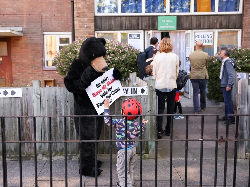 ناشط يرتدي زي دب يحمل لافتة خارج مركز اقتراع خلال الانتخابات العامة في لندن. 4 يوليو 2024 - REUTERS