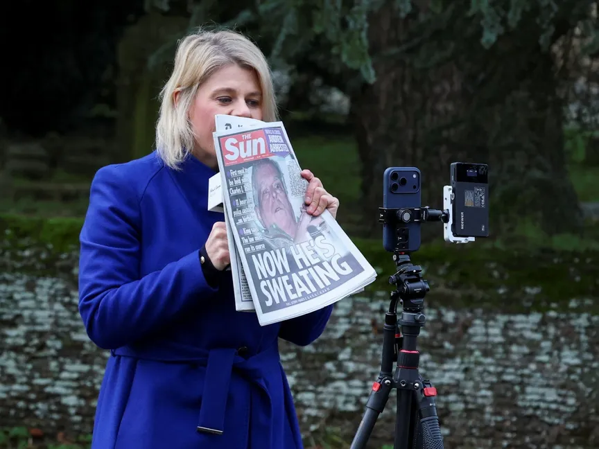 إعلامية بريطانية تحمل صحيفة على غلافها صورة الأمير السابق أندرو خارج قصر ساندرينجهام شمال مقاطعة نورفولك شرق إنجلترا. 20 فبراير 2026 - REUTERS