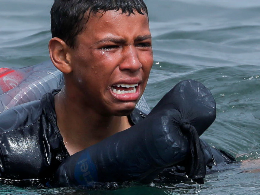 طفل مغربي يبكي وهو يسبح مستخدماً الزجاجات كعوامة، بالقرب من السياج الفاصل بين المغرب ومدينة سبتة التي تسيطر عليها إسبانيا، 19 مايو 2021. - REUTERS