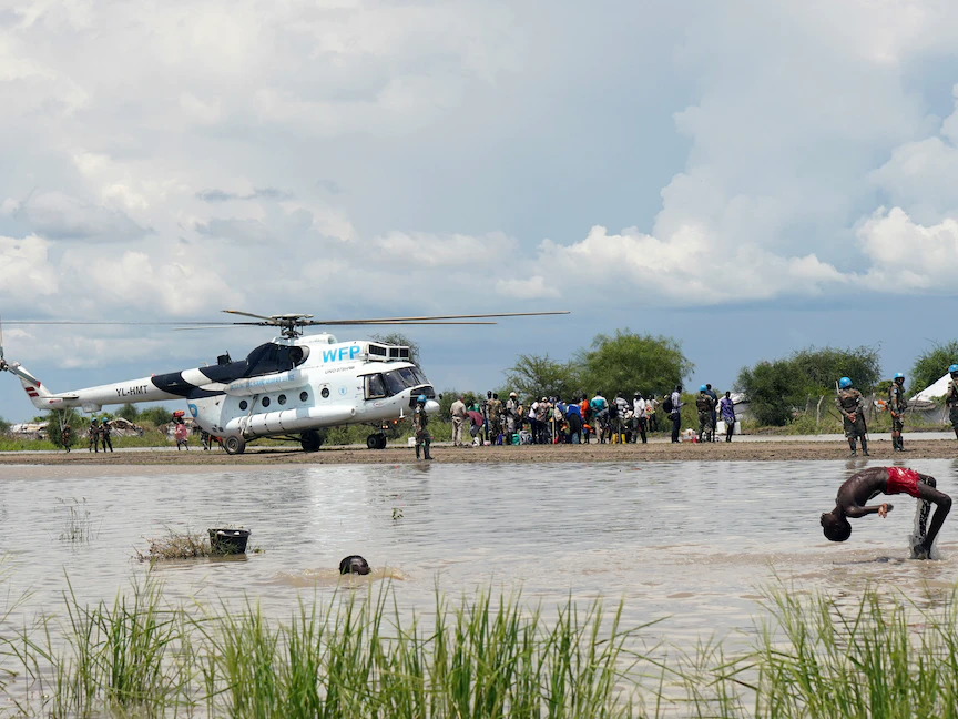 أطفال يلعبون في مياه الفيضانات عند مهبط طائرات بالقرب من مروحية تابعة لبرنامج الأغذية العالمي، في منطقة بيبور جنوب السودان، 6 أكتوبر 2020. - REUTERS