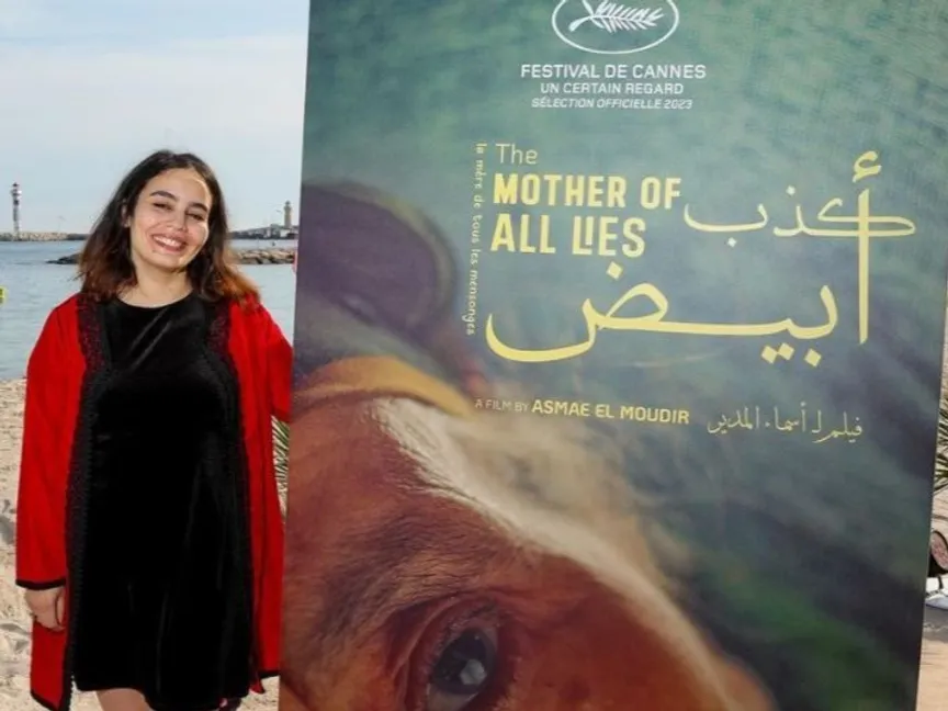 المخرجة المغربية أسماء المدير بجوار الملصق الدعائي لفيلمها الوثائقي "كدب أبيض" في الدورة 76 لمهرجان كان السينمائي - instagram/redseafilm