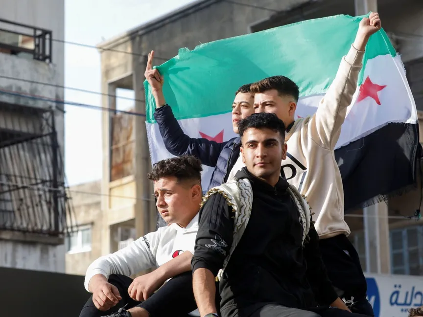 سوريون يحملون الأعلام بعد أن استولت الفصائل المسلحة على دمشق وأطاحوا بالرئيس السوري في محافظة اللاذقية. 9 ديسمبر 2024 - Reuters