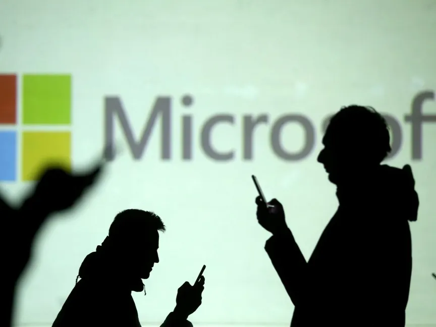 صورة تعبيرية لأشخاص يتابعون هواتفهم المحمولة وفي الخلفية شعار شركة مايكروسوفت الأميركية - REUTERS