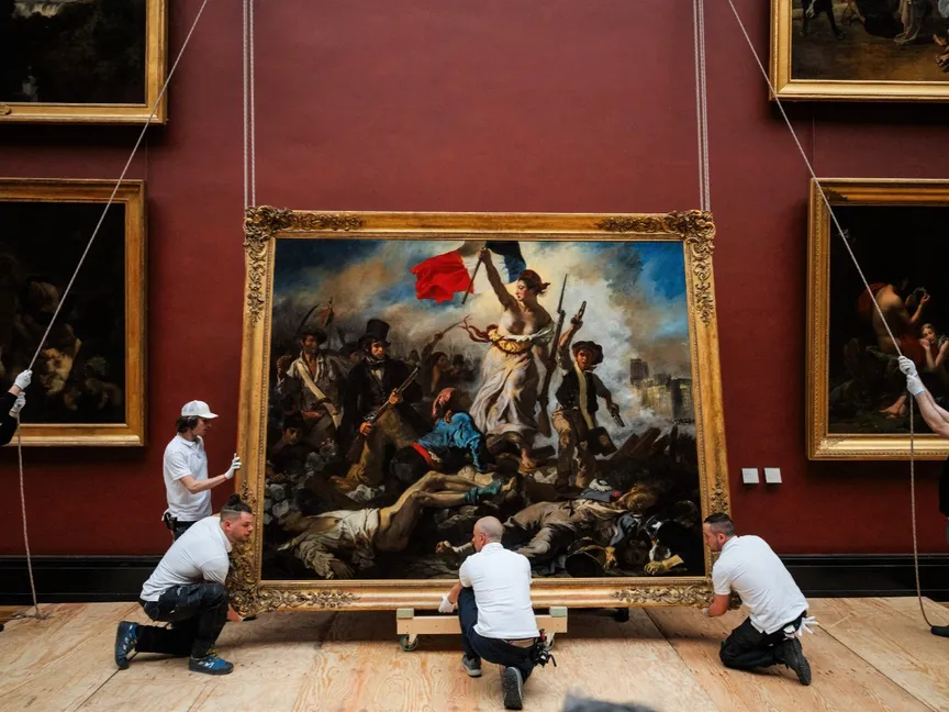 موظفو متحف اللوفر يعلّقون لوحة "الحرية تقود الشعب" (1830) للفنان الفرنسي يوجين ديلاكروا. 30 أبريل 2024 - AFP