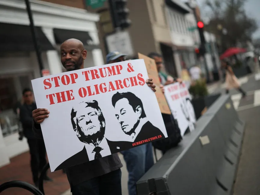 متظاهر يحمل لافتة عليها صور الرئيس التنفيذي لشركة تسلا إيلون ماسك والرئيس الأميركي دونالد ترمب خلال احتجاج خارج وكالة تسلا في حي جورج تاون في واشنطن العاصمة. 29 مارس 2025 - reuters