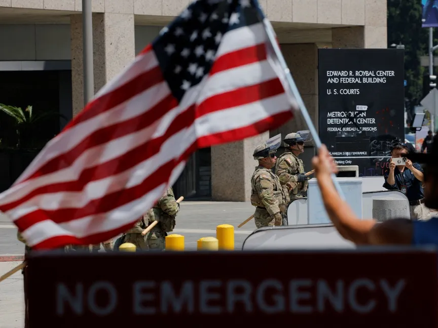 رجل يلوح بعلم الولايات المتحدة، بينما يقف أفراد من الحرس الوطني في كاليفورنيا حراسة خارج مبنى إدوارد آر. رويال الفيدرالي، بعد أيام من الاحتجاجات ضد حملات الهجرة الفيدرالية، ونشر الحرس الوطني في كاليفورنيا ومشاة البحرية الأميركية، في وسط مدينة لوس أنجلوس، كاليفورنيا، الولايات المتحدة، 10 يونيو 2025 - REUTERS