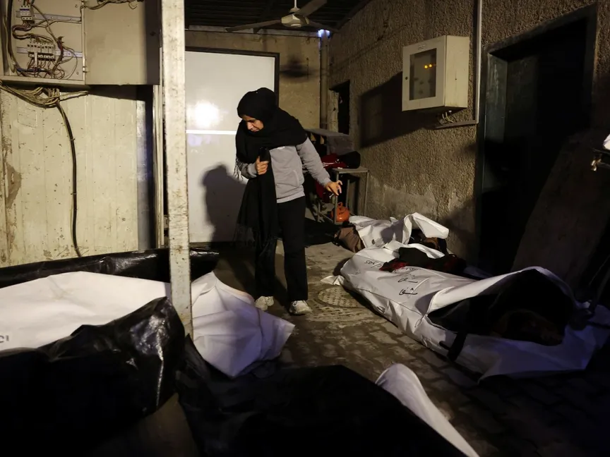 امرأة تمشي بجوار جثامين يعتقد أنها لسجناء من سجن صيدنايا، في مستشفى المجتهد في دمشق. 10 ديسمبر 2024 - Reuters