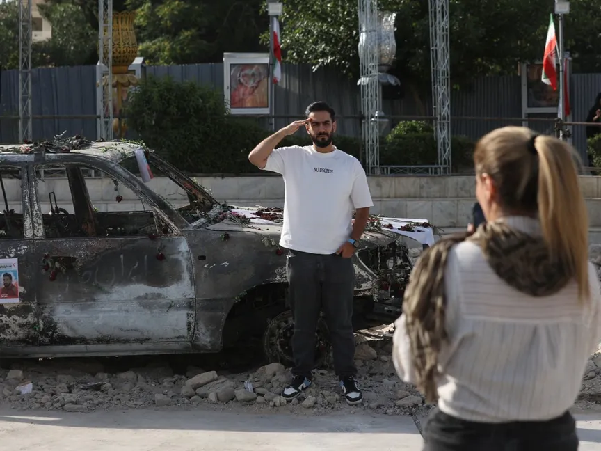 رجل يقف لالتقاط صورة بجوار سيارة إسعاف محترقة بأحد شوارع العاصمة طهران. 23 يونيو 2025 - REUTERS