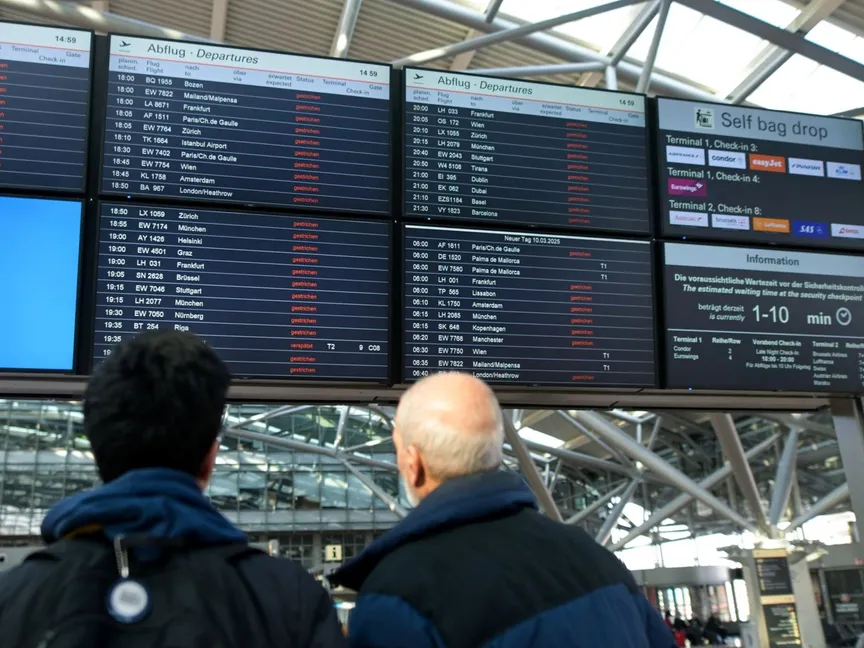 أشخاص يراقبون لوحات إلكترونية تعرض معلومات حول الرحلات الملغاة في مطار هامبورج، خلال إضراب مبكر غير متوقع يؤثر على الركاب، قبل يوم واحد من إضراب لمدة 24 ساعة في المطارات الألمانية دعا إليه اتحاد العمال الألماني فيردي بسبب نزاع على الأجور، في هامبورج، ألمانيا. 9 مارس 2025 - REUTERS