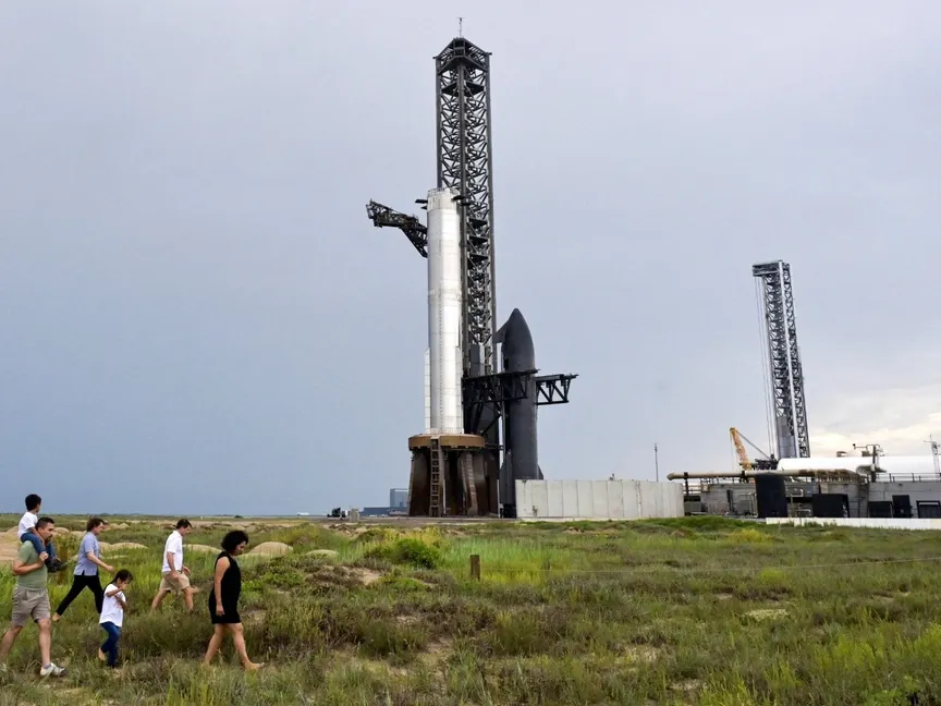 أميركيون يسيرون بالقرب من المركبة الفضائية SpaceX Starship المتصلة بمعزز ثقيل على منصة استعداداً للإطلاق في مجمع الشركة في ستاربيس، تكساس، الولايات المتحدة. 23 أغسطس 2025 - REUTERS