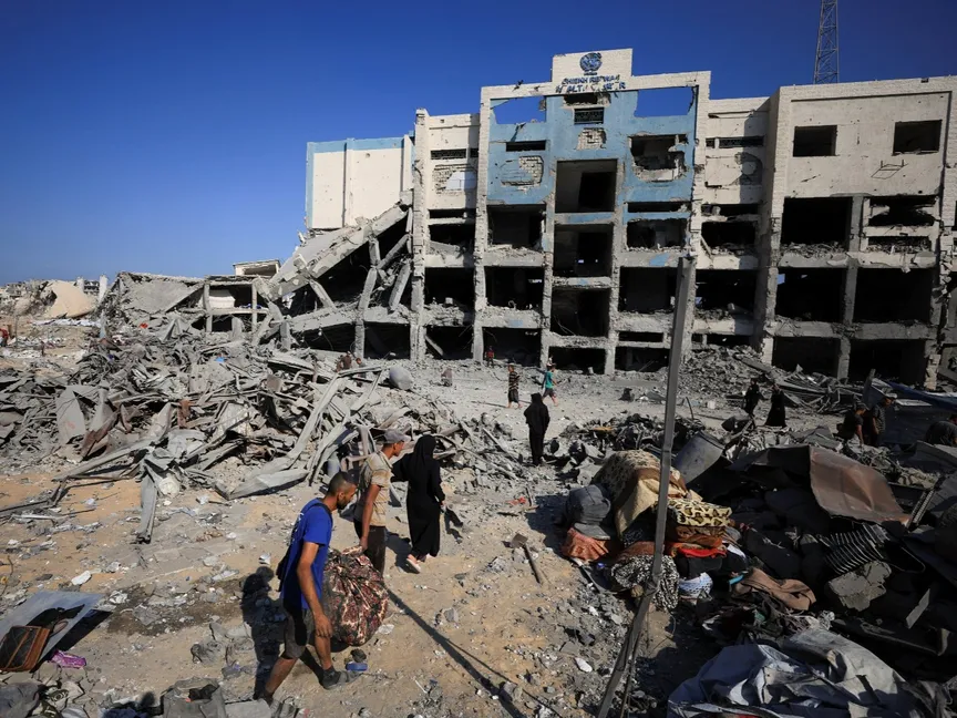 فلسطينيون يتفقدون الموقع المحيط بعيادة تابعة للأونروا كانت تأوي نازحين بعد استهدافها في غارة إسرائيلية في مدينة غزة. 6 أغسطس 2025 - Reuters