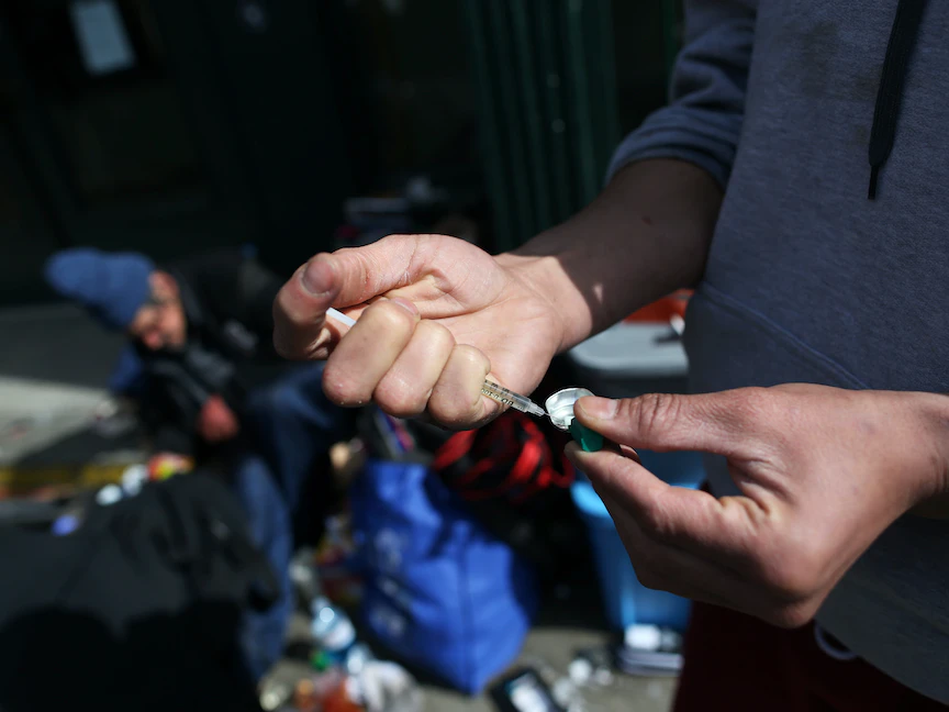 شخص يملأ حقنة بمواد مخدرة في أحد الشوارع وسط مدينة فانكوفر، كندا- 6 أبريل 2020 - REUTERS