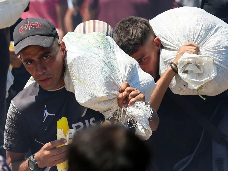 فلسطينيون يحملون أجولة من الدقيق قرب نقطة توزيع مساعدات، رفح، جنوب غزة. 24 يوليو 2025 - REUTERS