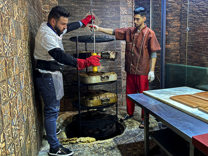 عامر حليمي يسحب صواني اللحم من فرن تحت الأرض في مطعمه في قسنطينة، الجزائر، في 12 مايو 2022 - REUTERS