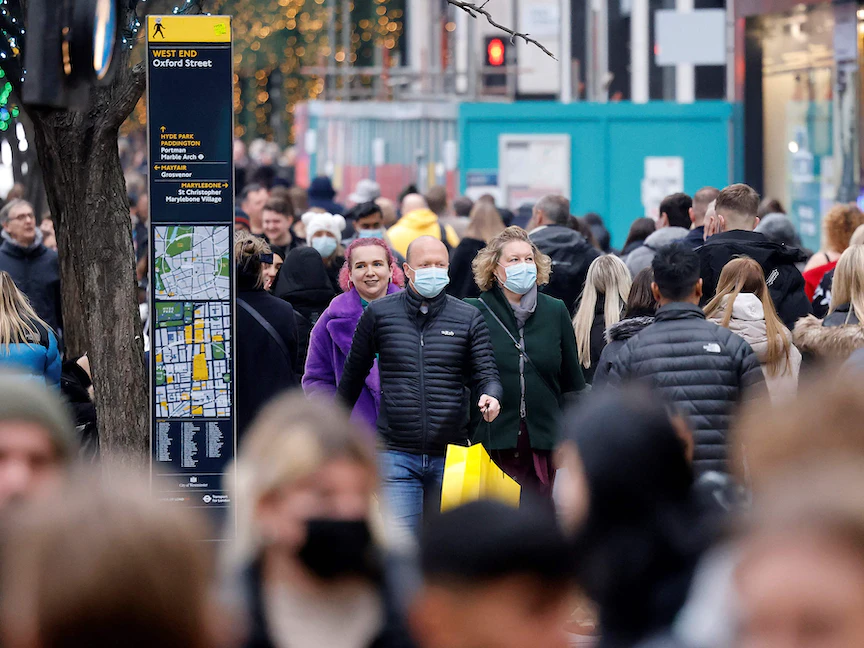 متسوقون بعضهم يضع كمامات يمرون بالقرب ممن متاجر في شارع أكسفورد بلندن. 18 ديسمبر 2021 - AFP