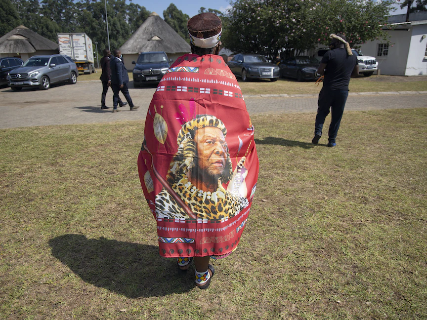 امرأة ترتدي راية عليها صورة لملك الزولو السابق زويليثيني، تمشي داخل القصر الملكي خلال حفل تأبينه في نونجوما - جنوب إفريقيا - 18 مارس 2021 - AFP