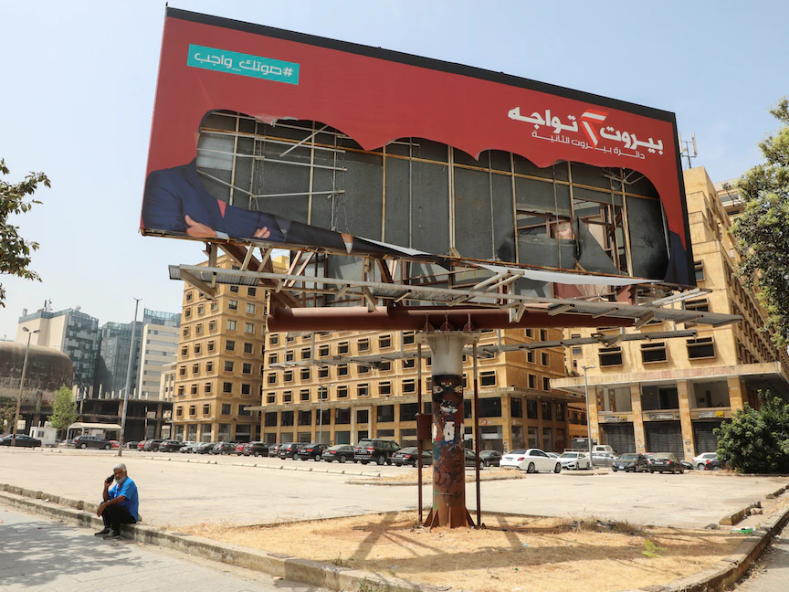 رجل يجلس قرب لافتة ممزقة لأحد المرشحين للانتخابات النيابية في بيروت- 27 أبريل 2022 - REUTERS