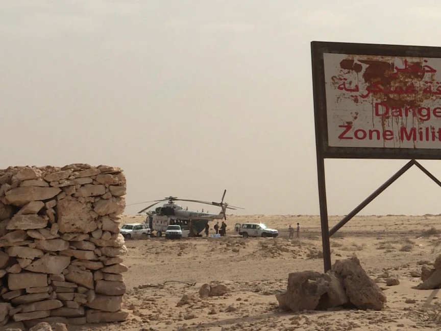 إشارة للجيش المغربي داخل المنطقة العازلة في الكركارات تقول "منطقة عسكرية" وفي الخلفية سيارات ومروحية تابعة لقوات "مينورسو" الأممية - الشرق