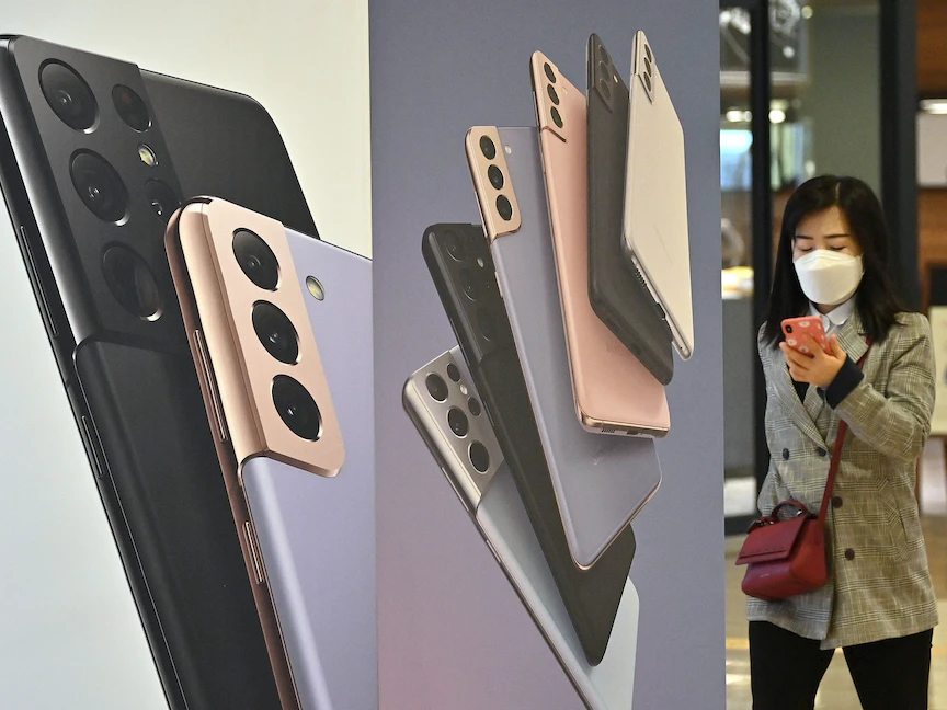سيدة تستخدم هاتفها أمام إعلان لهواتف سامسونغ غلاكسي S21 في صالة عرض للشركة في سيول، 7 أبريل 2021 - AFP