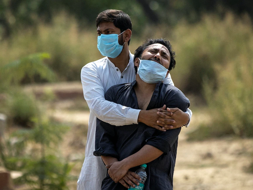 رجل يواسي قريبه الذي يرى جثة والده المتوفى متأثراً بكورونا في مقبرة بنيودلهي، الهند- 16 أبريل 2021. - REUTERS