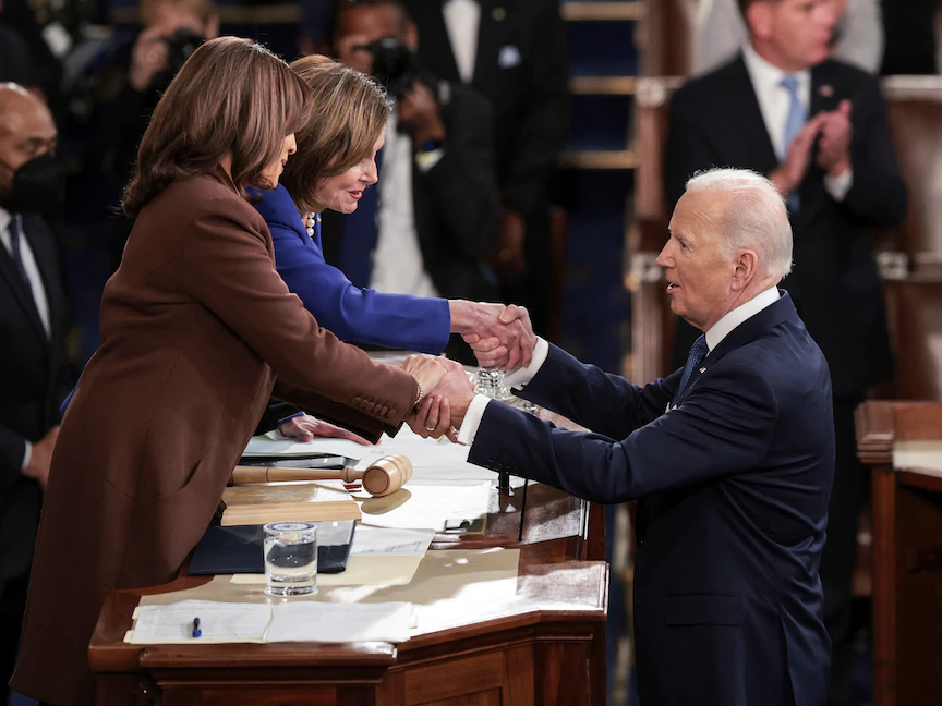 الرئيس الأميركي جو بايدن يمسك بيدي رئيس مجلس النواب نانسي بيلوسي ونائبته كامالا هارس - 01 مارس 2022 - REUTERS