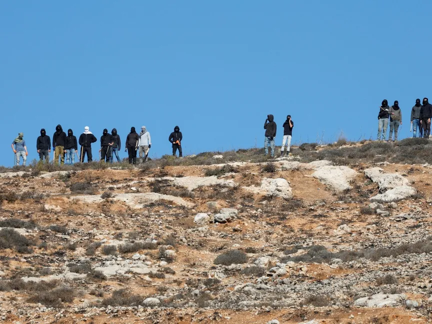 مستوطنون إسرائيليون يراقبون الجنود الإسرائيليون وهم يمنعون المزارعين الفلسطينيين من الوصول لمزارع الزيتون في برقة القريبة من رام الله بالضفة الغربية. 20 أكتوبر 2024 - REUTERS
