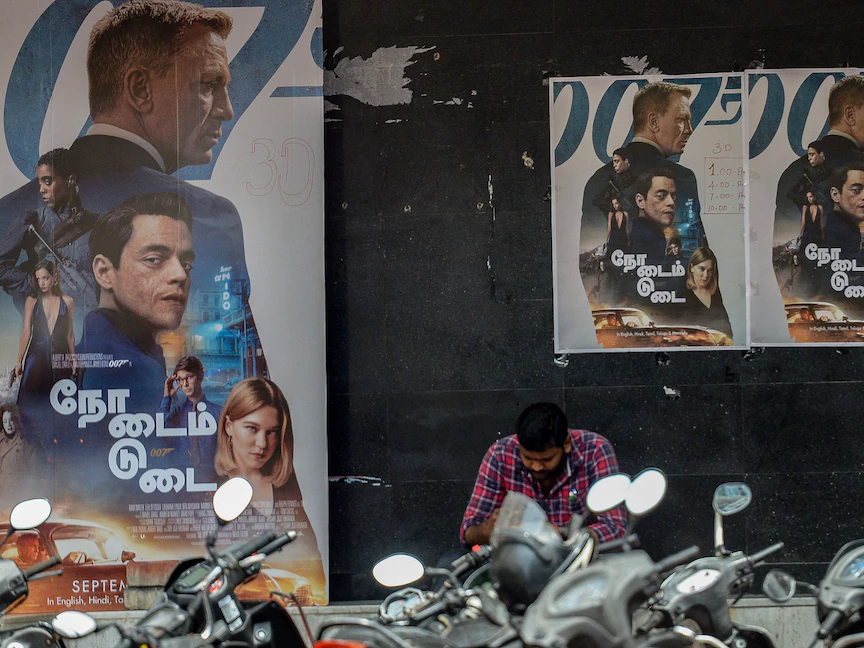 رجل يجلس بجانب ملصق لأحدث أفلام جيمس بوند "لا وقت للموت" خارج قاعة سينما في تشيناي، الهند، 30 سبتمبر 2021 - AFP