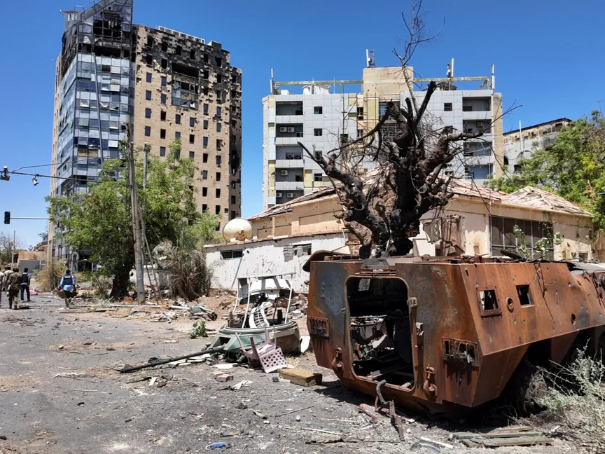 أفراد من الجيش السوداني يسيرون بالقرب من مركبة عسكرية مدمرة ومبانٍ تعرضت للقصف في الخرطوم. 26 مارس 2025 - REUTERS