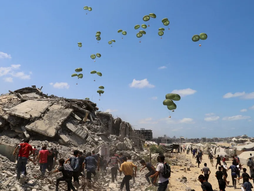 فلسطينيون يركضون نحو المظلات التي تحمل مساعدات تم إسقاطها جواً فوق شمال قطاع غزة. 7 أغسطس 2025 - reuters