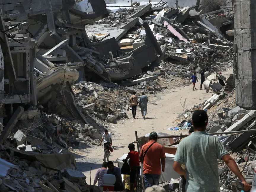 أشخاص يسيرون على طريق بين أنقاض المباني التي دمرها القصف الإسرائيلي في خان يونس بجنوب قطاع غزة. 23 يونيو 2024 - AFP