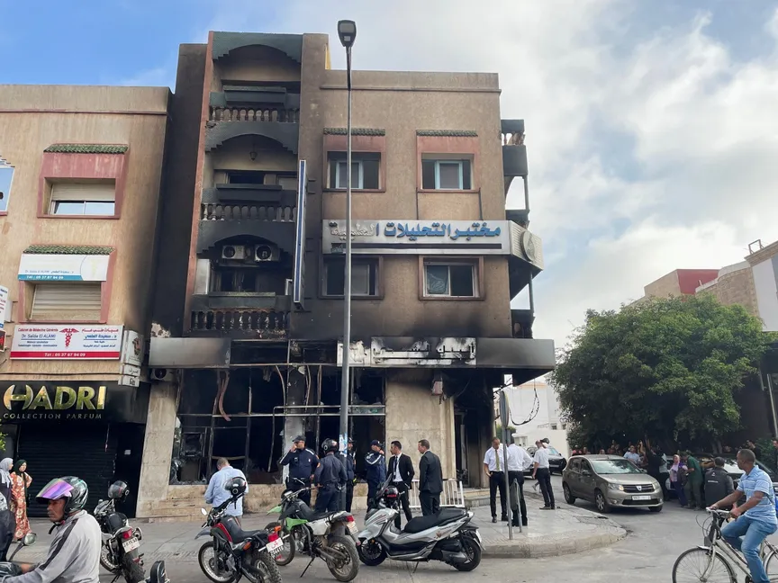 أشخاص يقفون بجانب مبنى محترق كان يضم بنكاً وذلك عقب احتجاجات مناهضة للحكومة قادها شباب، في مدينة سلا بالمغرب. 2 أكتوبر 2025 - Reuters