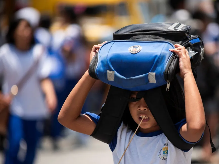 طالبة تستخدم حقيبتها المدرسية للاحتماء من أشعة الشمس خارج مدرسة في مانيلا بالفلبين. 19 أبريل 2024 - Reuters