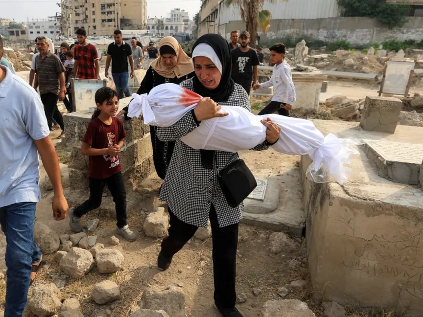 امرأة فلسطينية تحمل جثمان حفيدتها التي قتلها إسرائيل في غارة جوية لدفنها في مقبرة بمدينة غزة. 13 أغسطس 2025 - Reuters