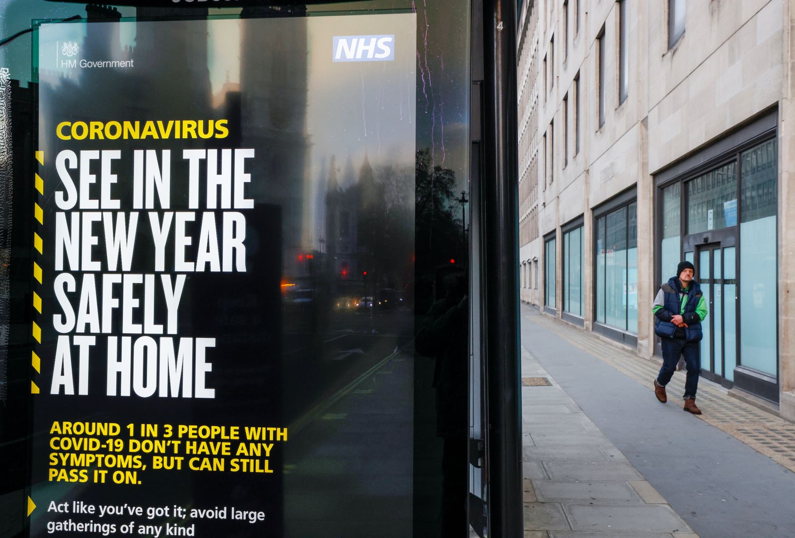 رجل يمشي أمام لافتة إعلان للحكومة البريطانية تذكر الناس بالبقاء في المنزل في العام الجديد في لندن، 31 ديسمبر 2020 - REUTERS