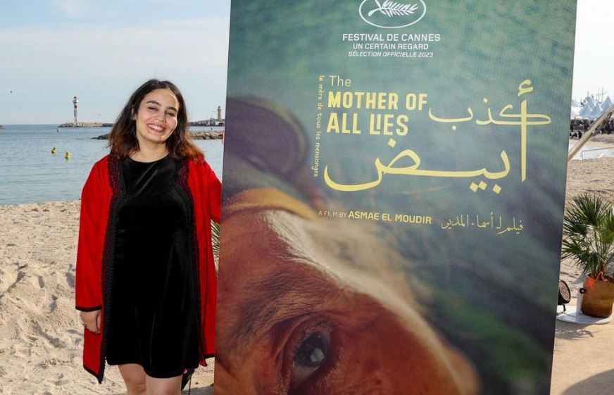 المخرجة المغربية أسماء المدير بجوار الملصق الدعائي لفيلمها الوثائقي 